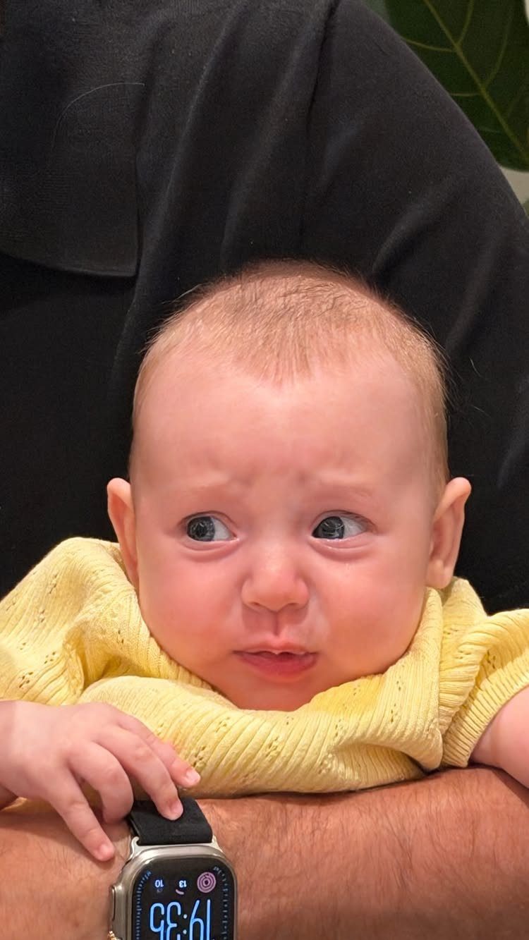 Baby in a yellow knitted sweater held by an adult wearing a watch.