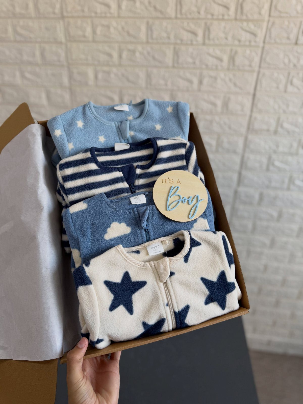 Four folded baby fleece jackets with stars and stripes in a cardboard box.
