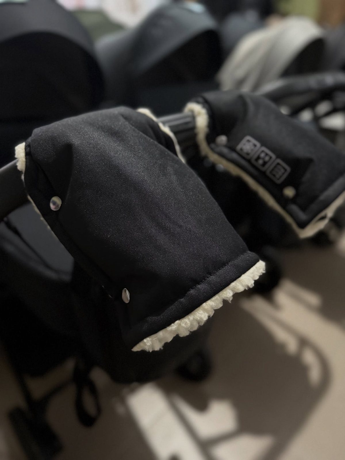 Black fabric hand warmers with white fleece lining attached to a stroller handle.