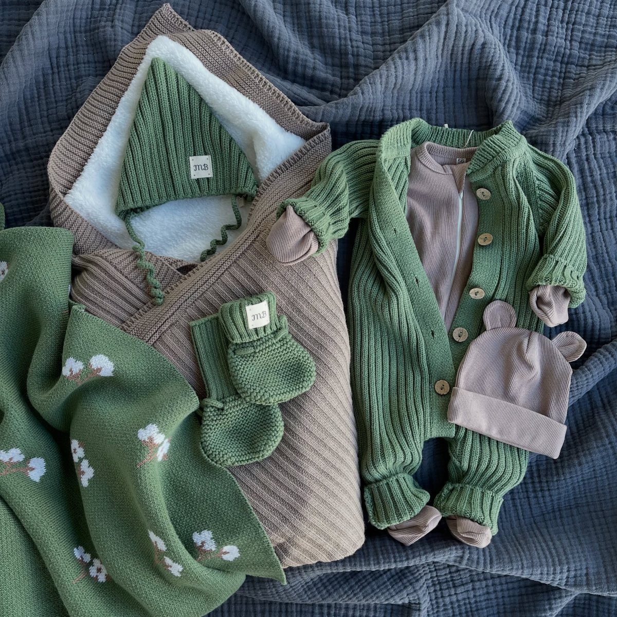 Newborn cold weather clothes including a green romper, bunting bag, and knitted accessories.