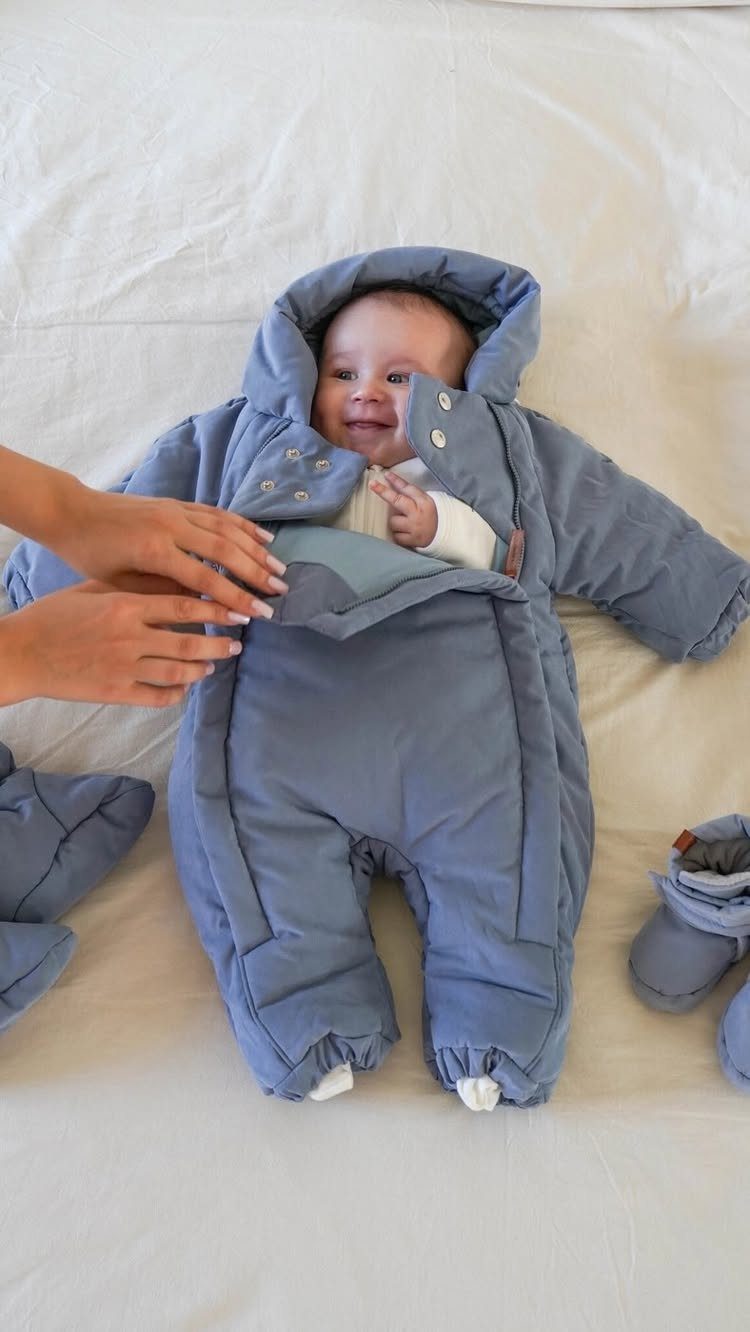 Newborn baby wearing a padded blue winter snowsuit lying on a white blanket