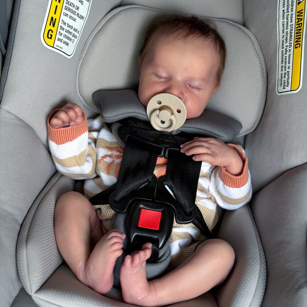 Newborn baby sleeping in a grey car seat wearing thin striped clothing