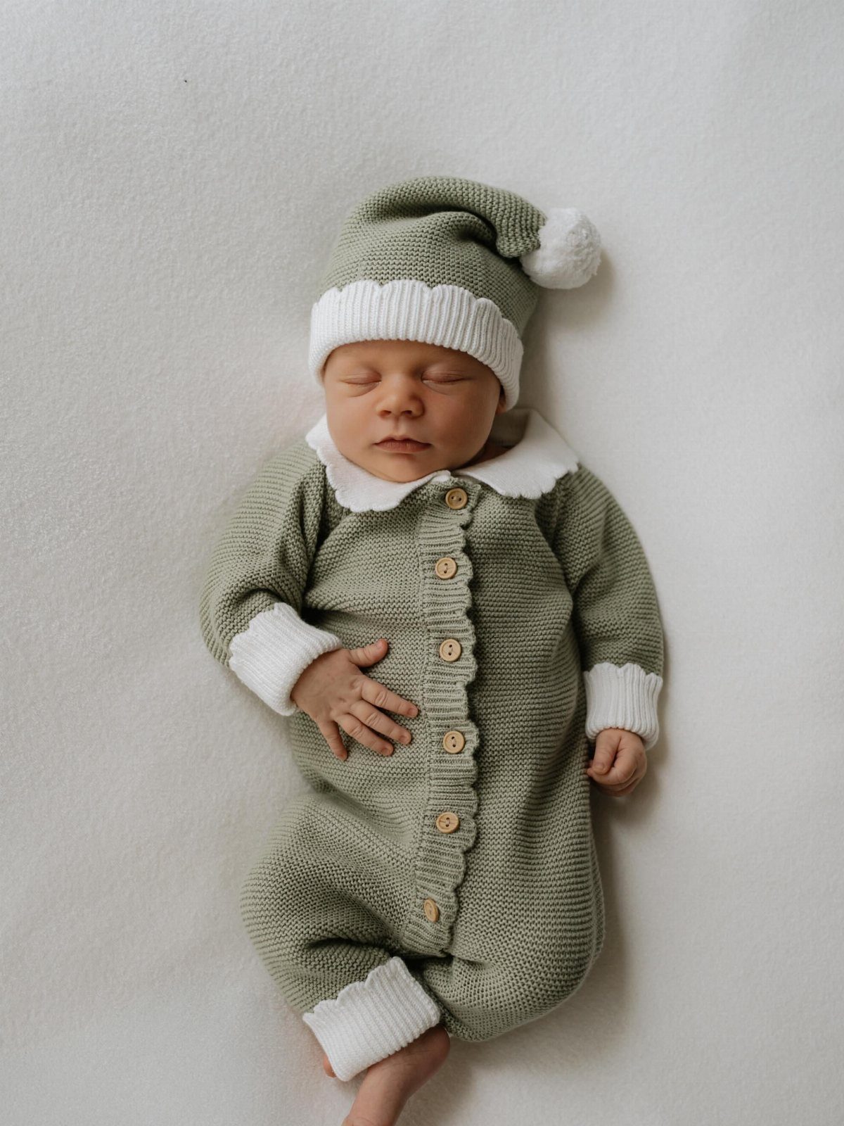 Sleeping newborn baby wearing a sage green knitted elf outfit and matching hat.