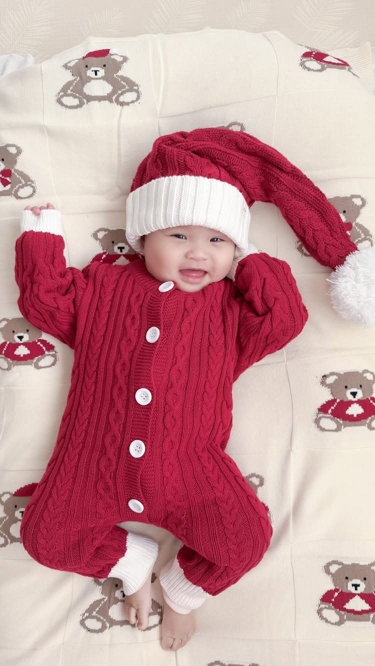 Smiling baby wearing a red cable-knit Santa romper and matching knit hat.