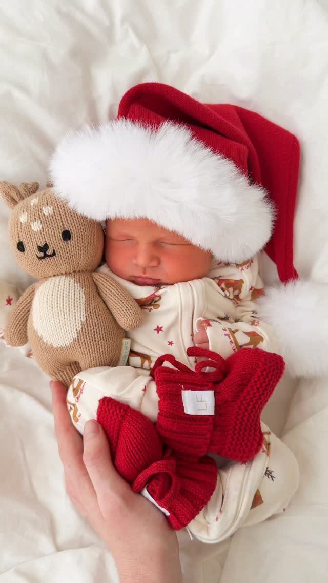 Sleeping newborn baby in a Santa hat and patterned romper with a deer toy.