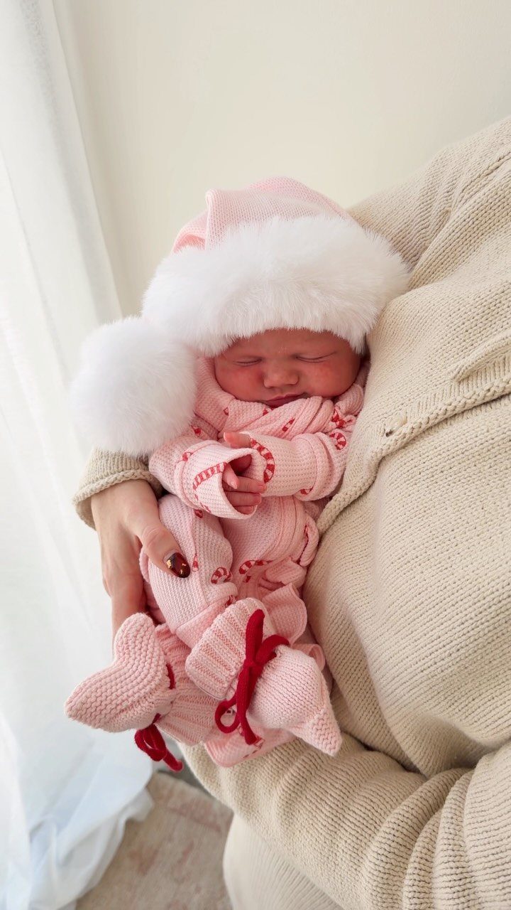 Newborn baby in a pink knitted Christmas outfit and faux-fur Santa hat.