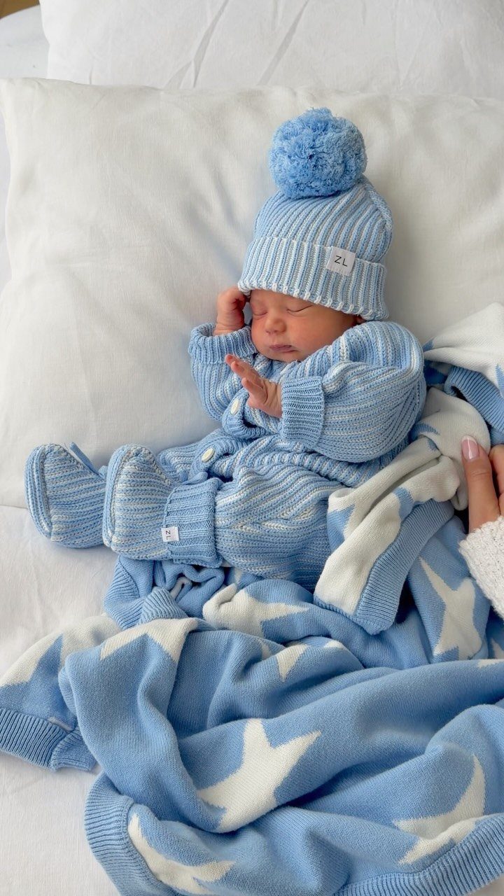 Sleeping newborn baby wearing a light blue knitted outfit and matching beanie hat.