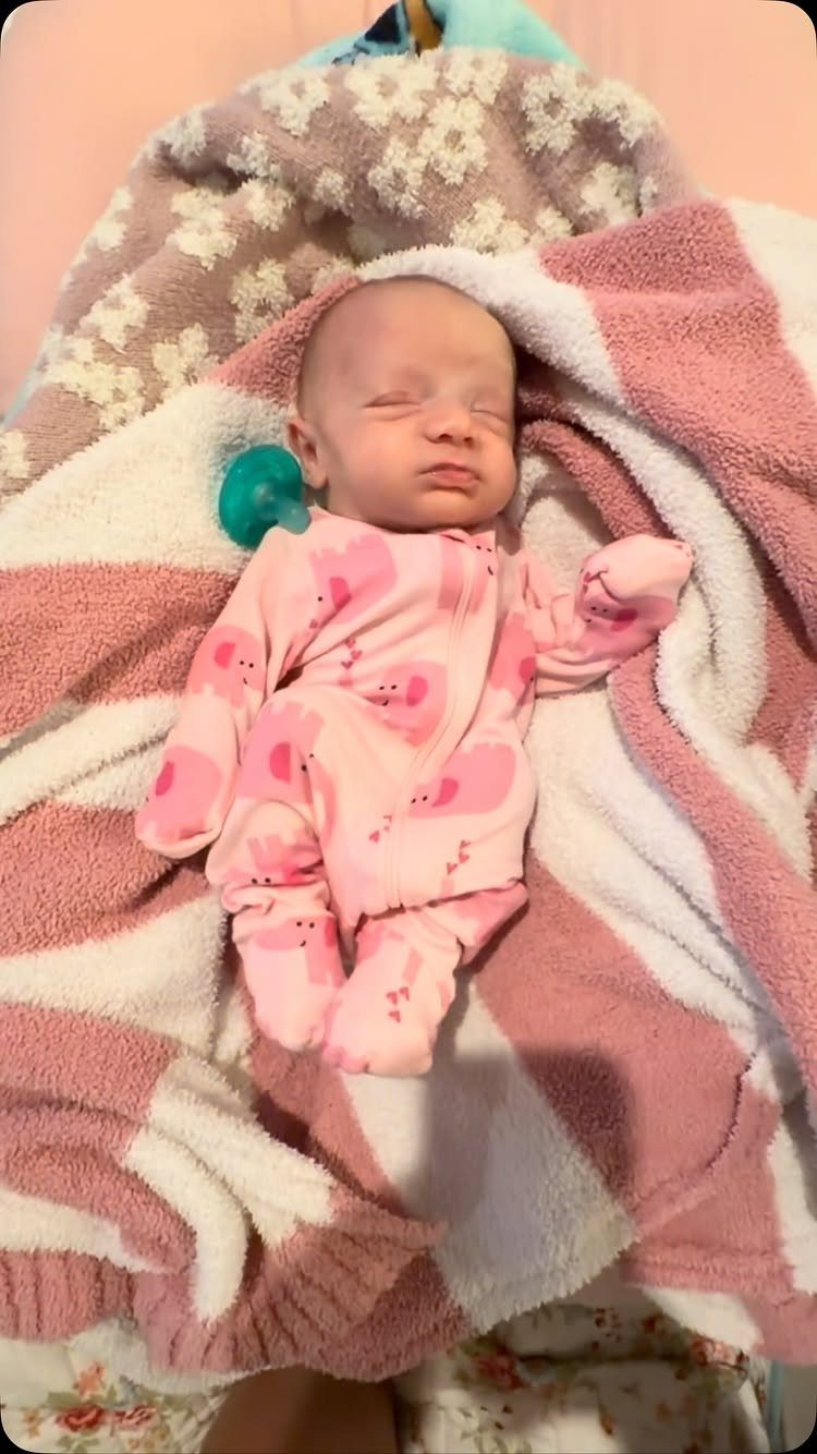 Sleeping newborn baby wearing a pink patterned sleeper on a striped blanket