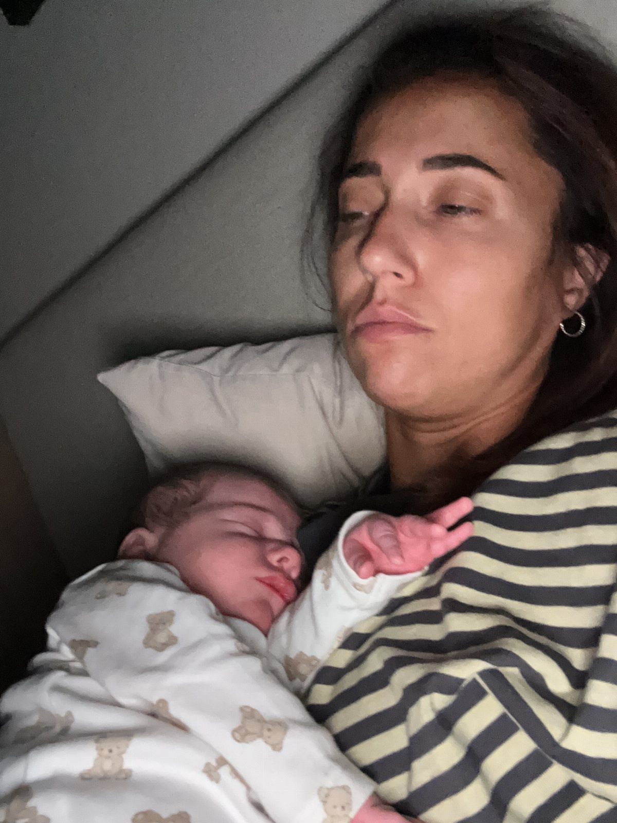 Woman in striped shirt holding a sleeping newborn wearing bear print clothes.