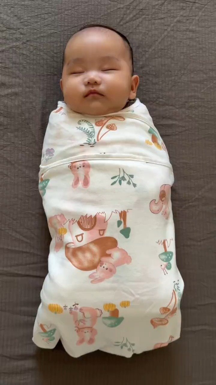Sleeping newborn baby wrapped in a white patterned swaddle blanket on grey fabric