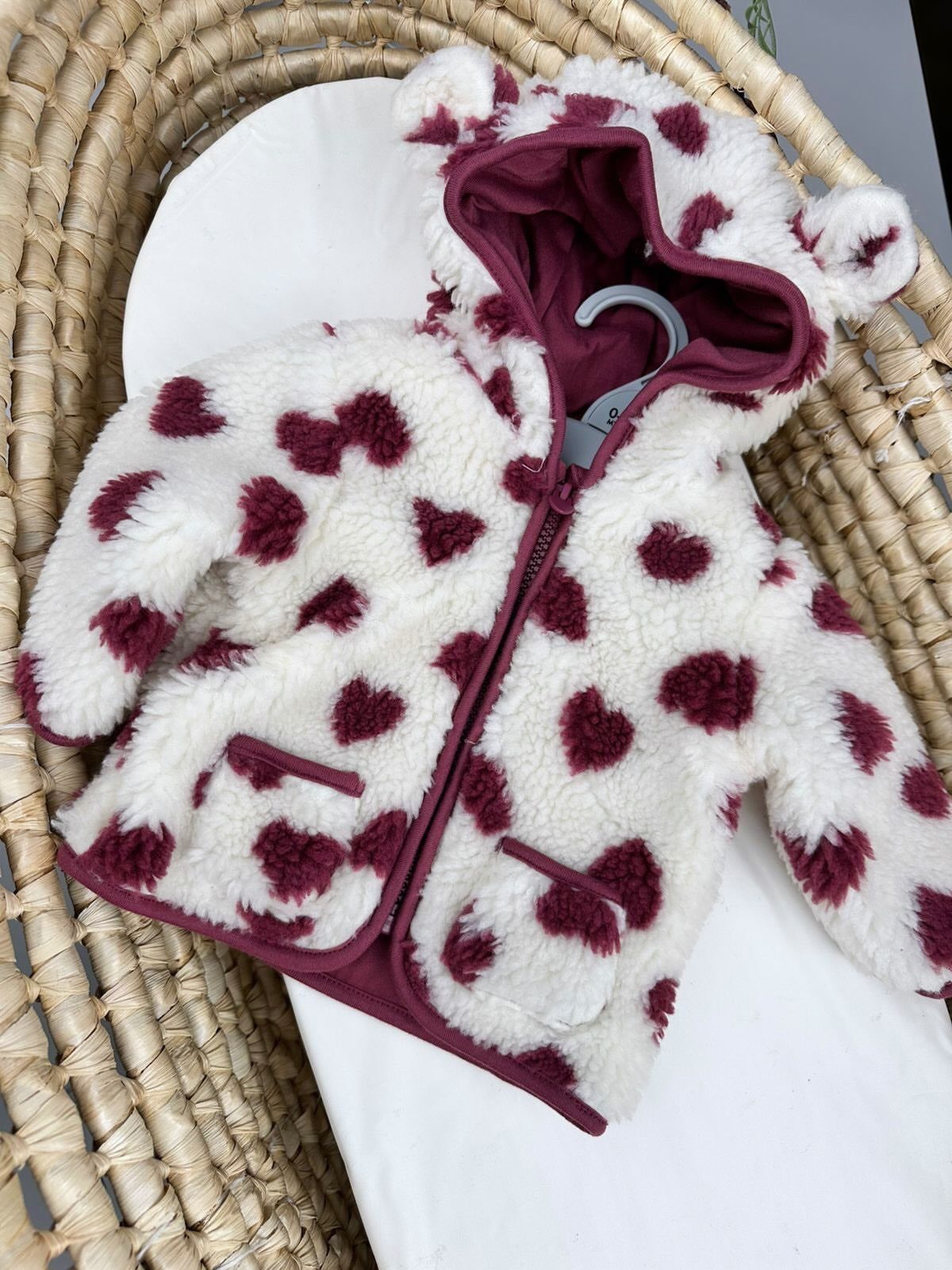White fluffy fleece baby jacket with maroon hearts and ears in a basket