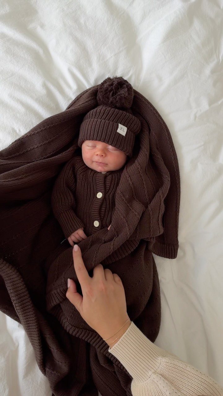 Newborn baby wearing brown knitted hat and cardigan wrapped in a brown blanket