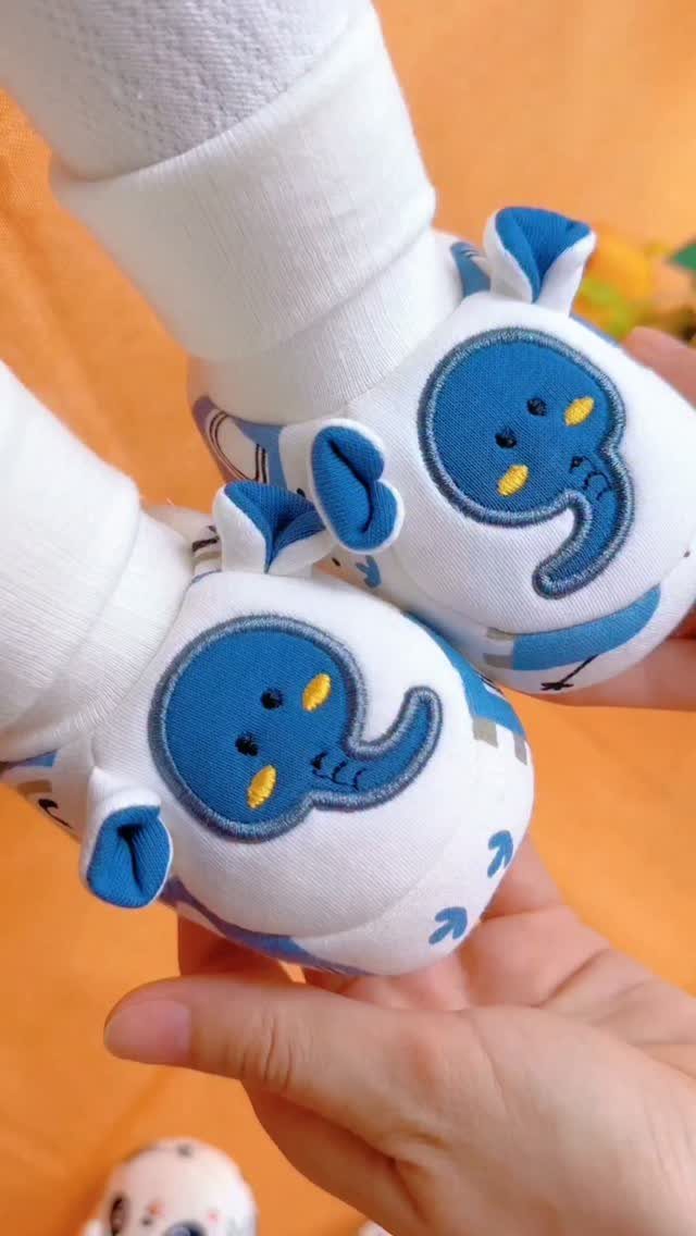 Baby feet wearing white shoes with blue elephant faces held by an adult hand.
