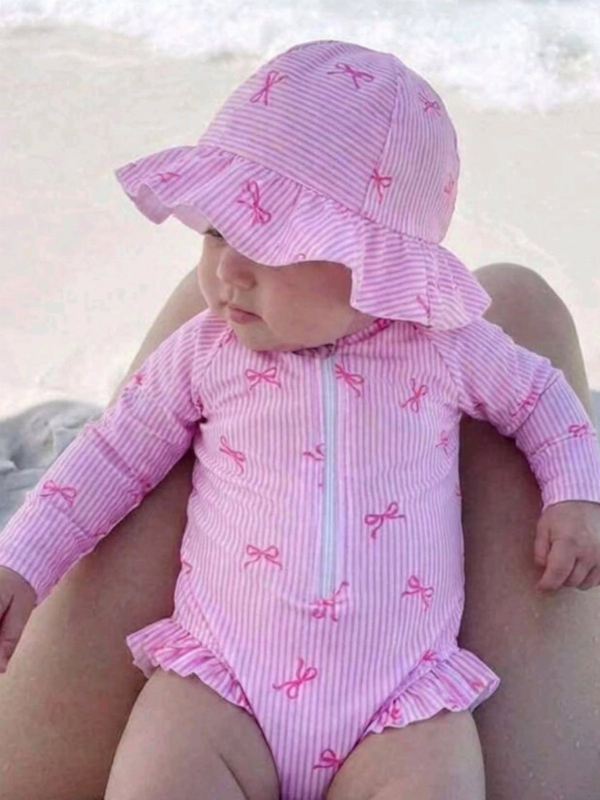 Baby in pink striped swimsuit and sun hat sitting on a sandy beach