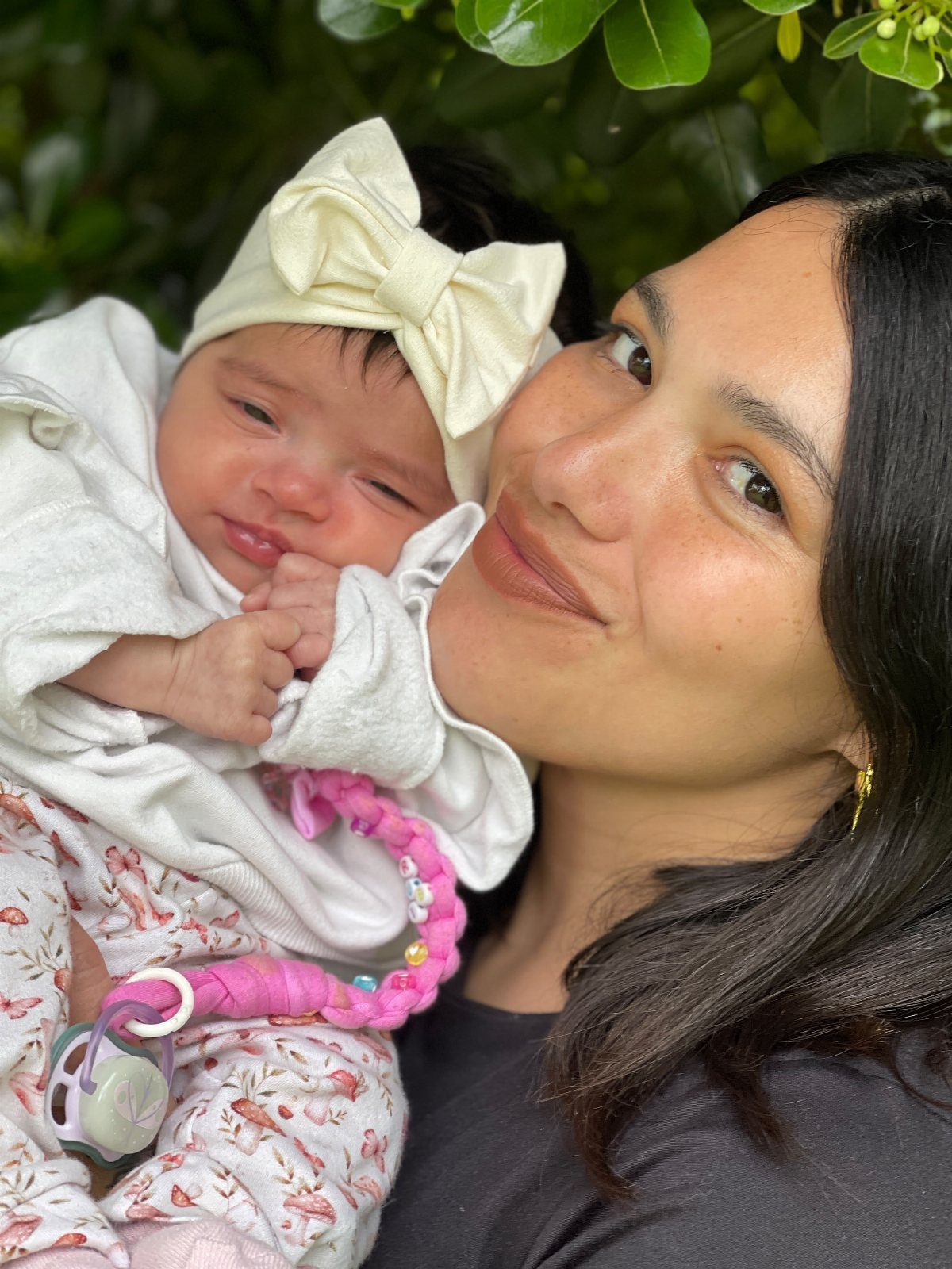 Woman smiling next to a newborn baby wearing a white jacket and floral leggings.