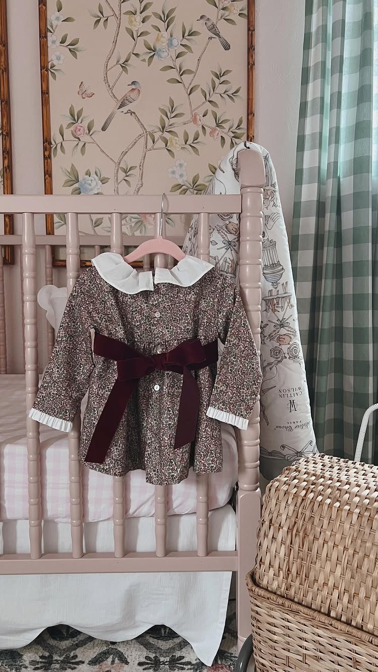 Floral baby girl dress with burgundy velvet bow hanging on a pink crib