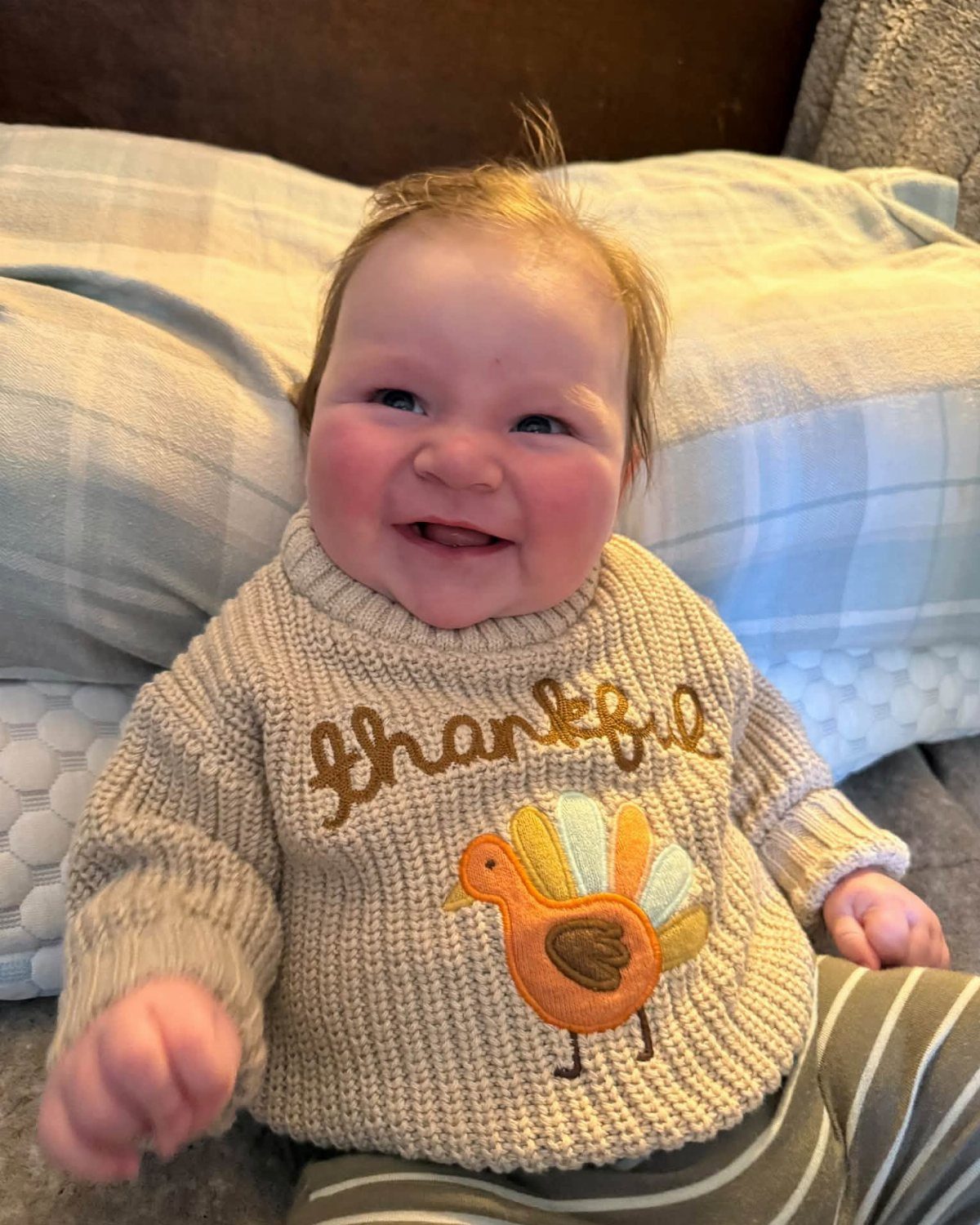 Smiling baby wearing a beige knit sweater with a turkey and Thankful text.