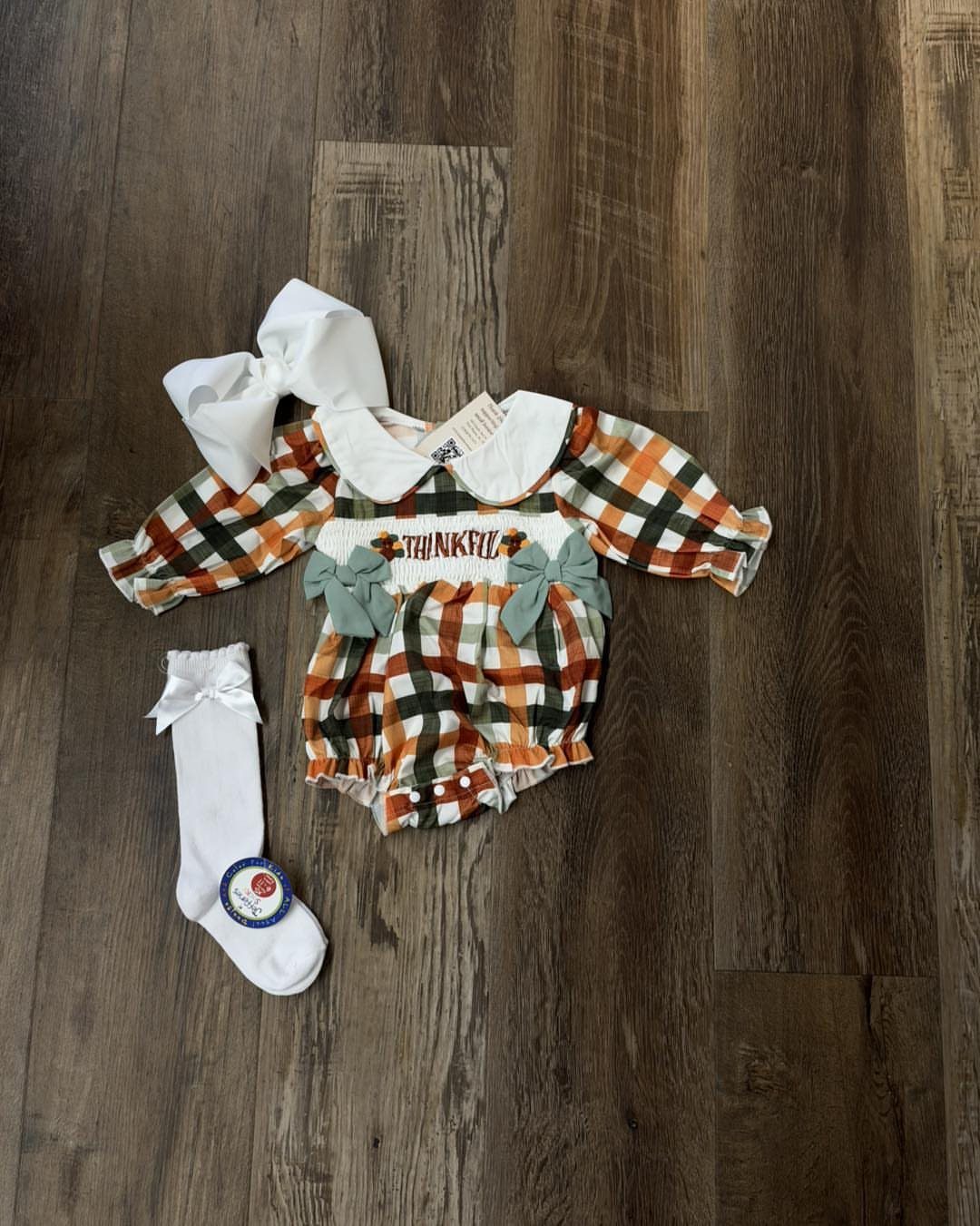 Plaid baby romper in orange and green with matching bow and sock.