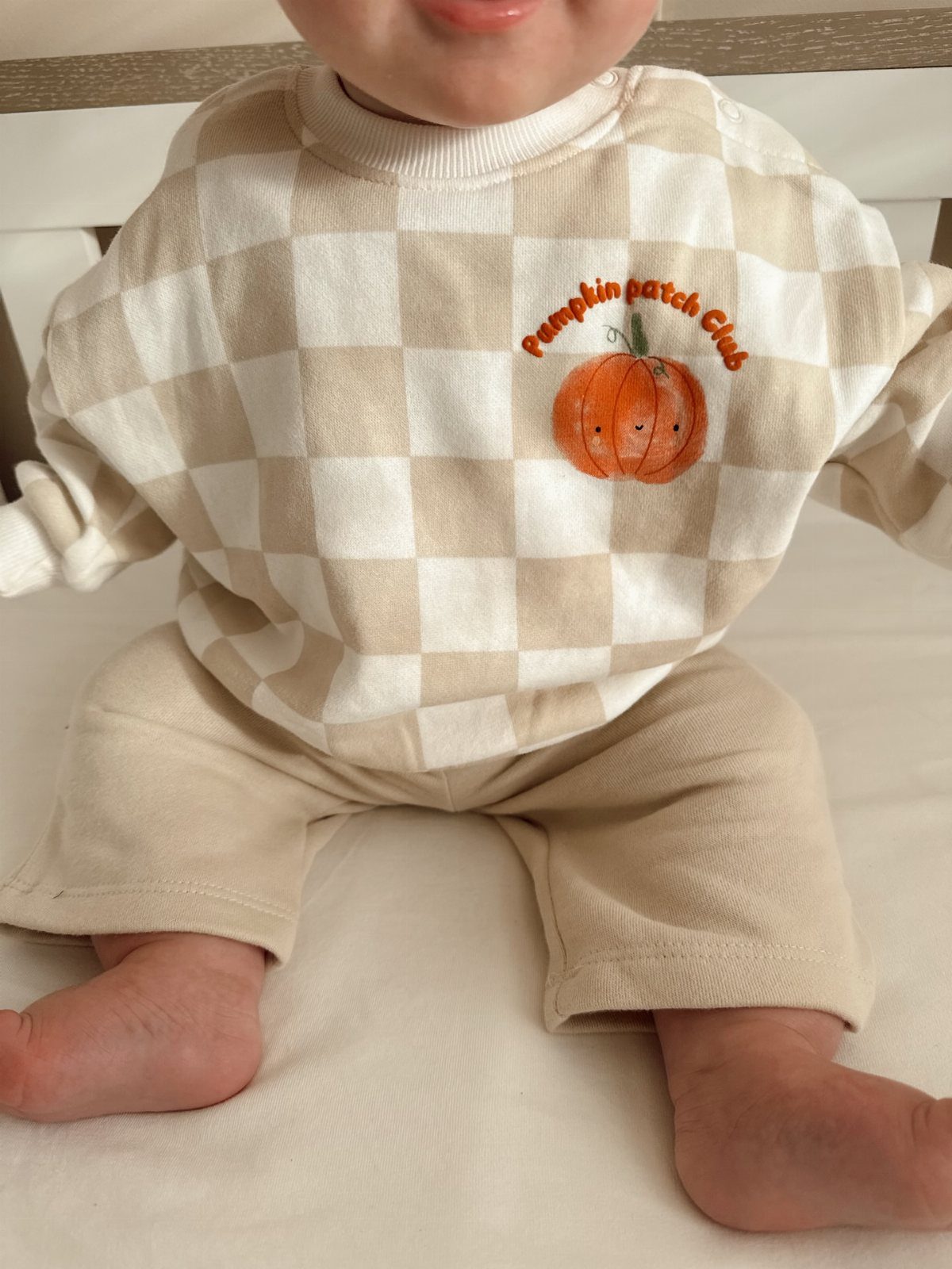Baby wearing a checkered pumpkin patch outfit with matching beige pants.