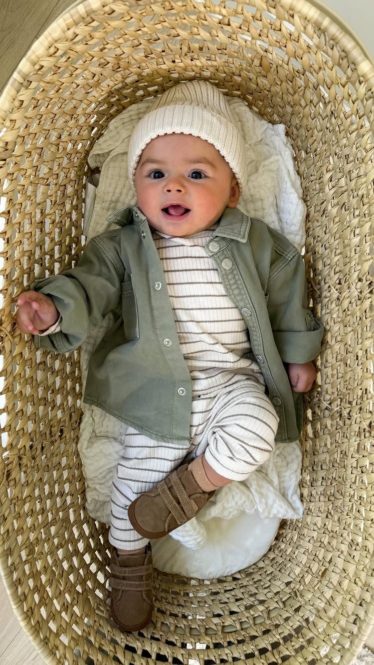 Baby in olive green shirt and knit beanie lying in a woven basket