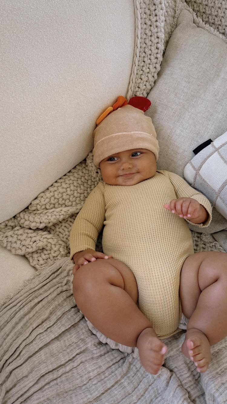 Newborn baby wearing a tan thanksgiving turkey outfit lying on beige blankets.