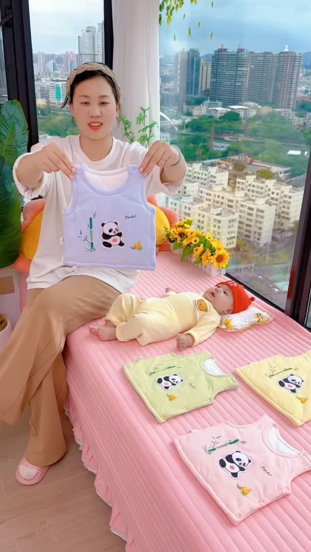 Woman holding a blue panda infant vest next to a baby in pajamas.
