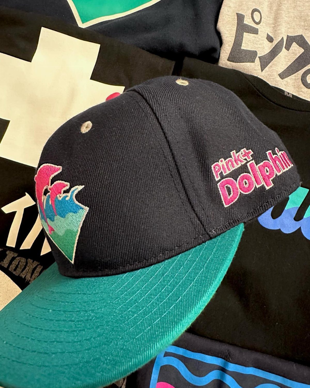 Pink Dolphin Clothing: 7 Ideas for Hoodies, Hats and More 6 Navy blue Pink+Dolphin baseball cap with teal brim resting on graphic t-shirts