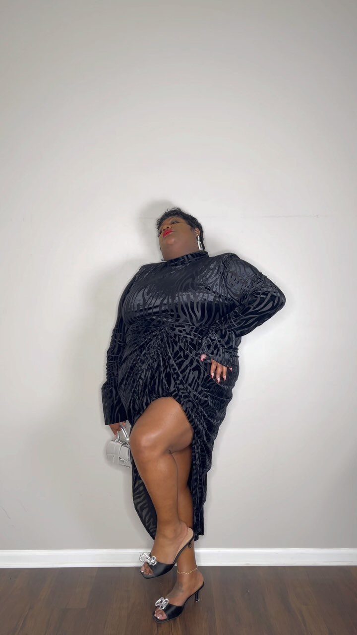 Plus-size woman wearing a long black textured velvet dress with a high leg slit.