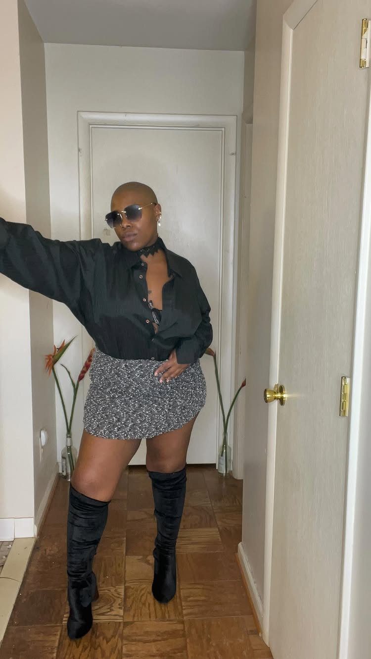 Plus-size person wearing a black shirt, patterned mini skirt, and black thigh-high boots.