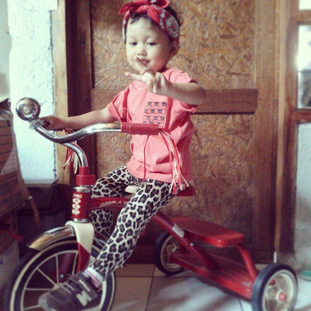 10 Rockabilly Infant Clothing Ideas for Little Rock Stars 8 Child in red fringe top and leopard leggings sitting on a red tricycle.