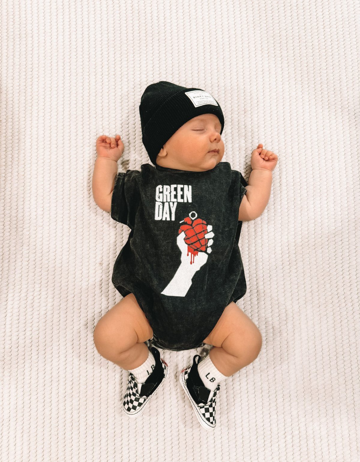 Rockstar Infant Clothing Ideas: 5 Looks for Little Rockers 3 Sleeping infant wearing a Green Day band bodysuit, black beanie, and checkered sneakers.