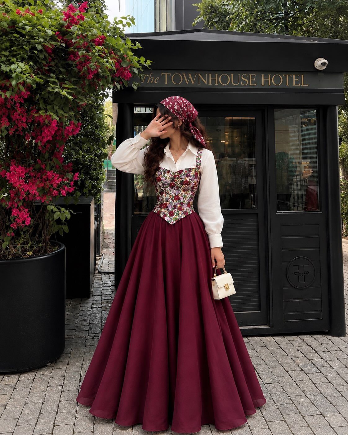 Woman in a floral corset bodice, burgundy skirt, and matching headscarf outdoors.