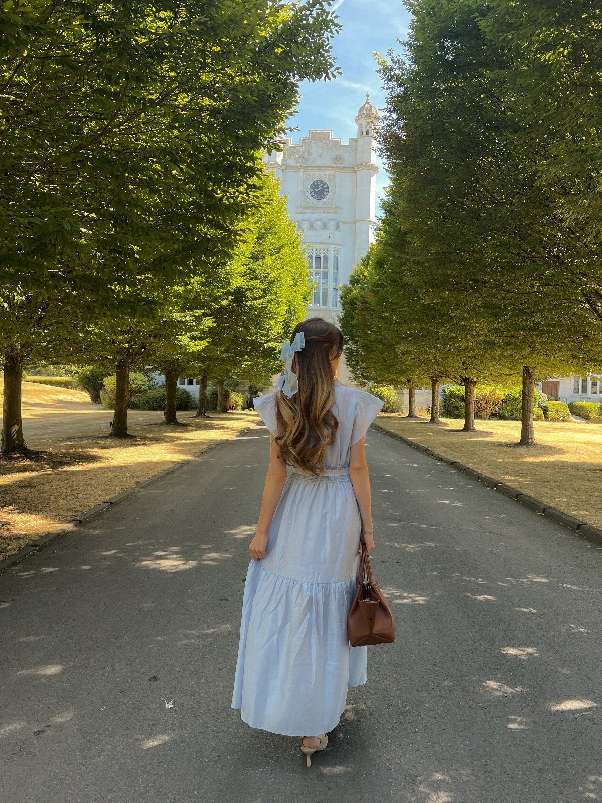 Woman in a light blue tiered romantic dress walking toward a white building