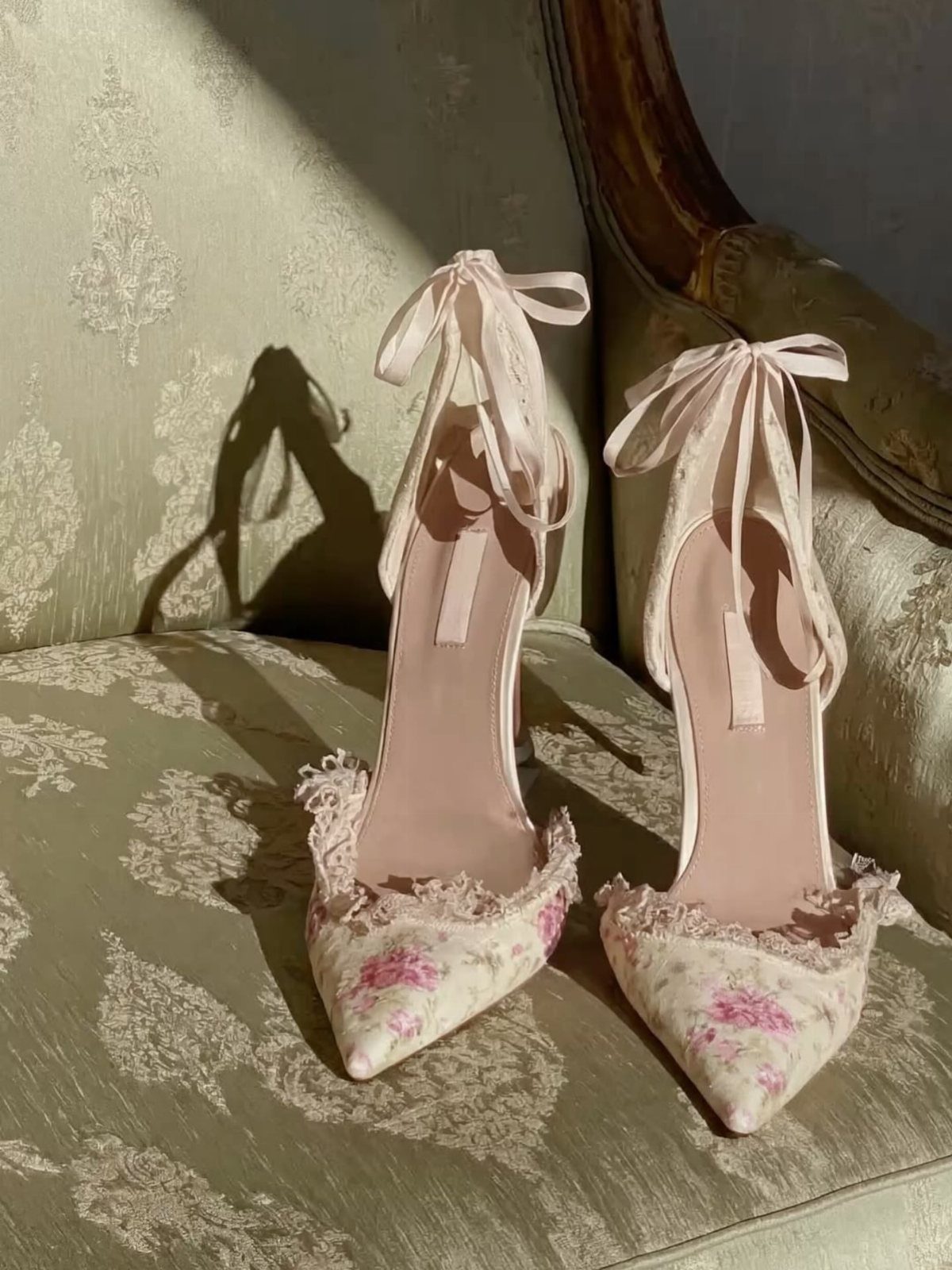 Floral pointed-toe high heels with lace trim and satin ankle ribbons on damask fabric.