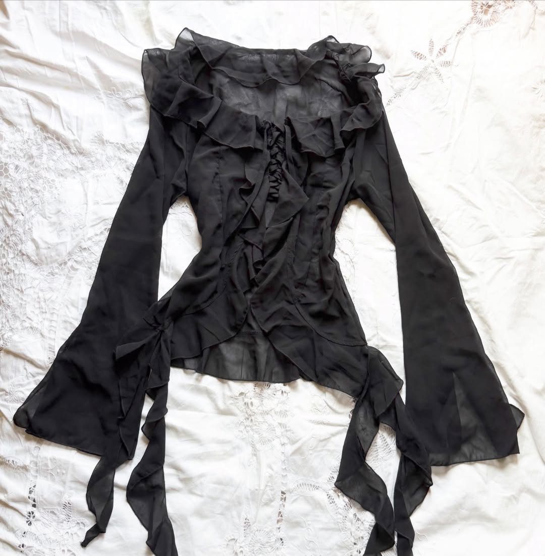 Black sheer ruffled blouse with flared sleeves on a white fabric background
