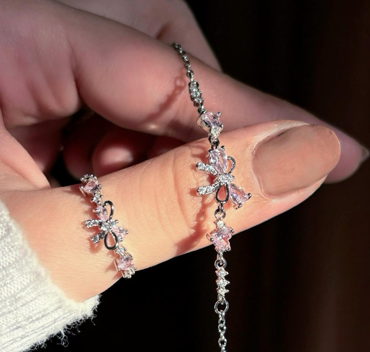 Thin silver ring and necklace with pink bow gemstones on a hand