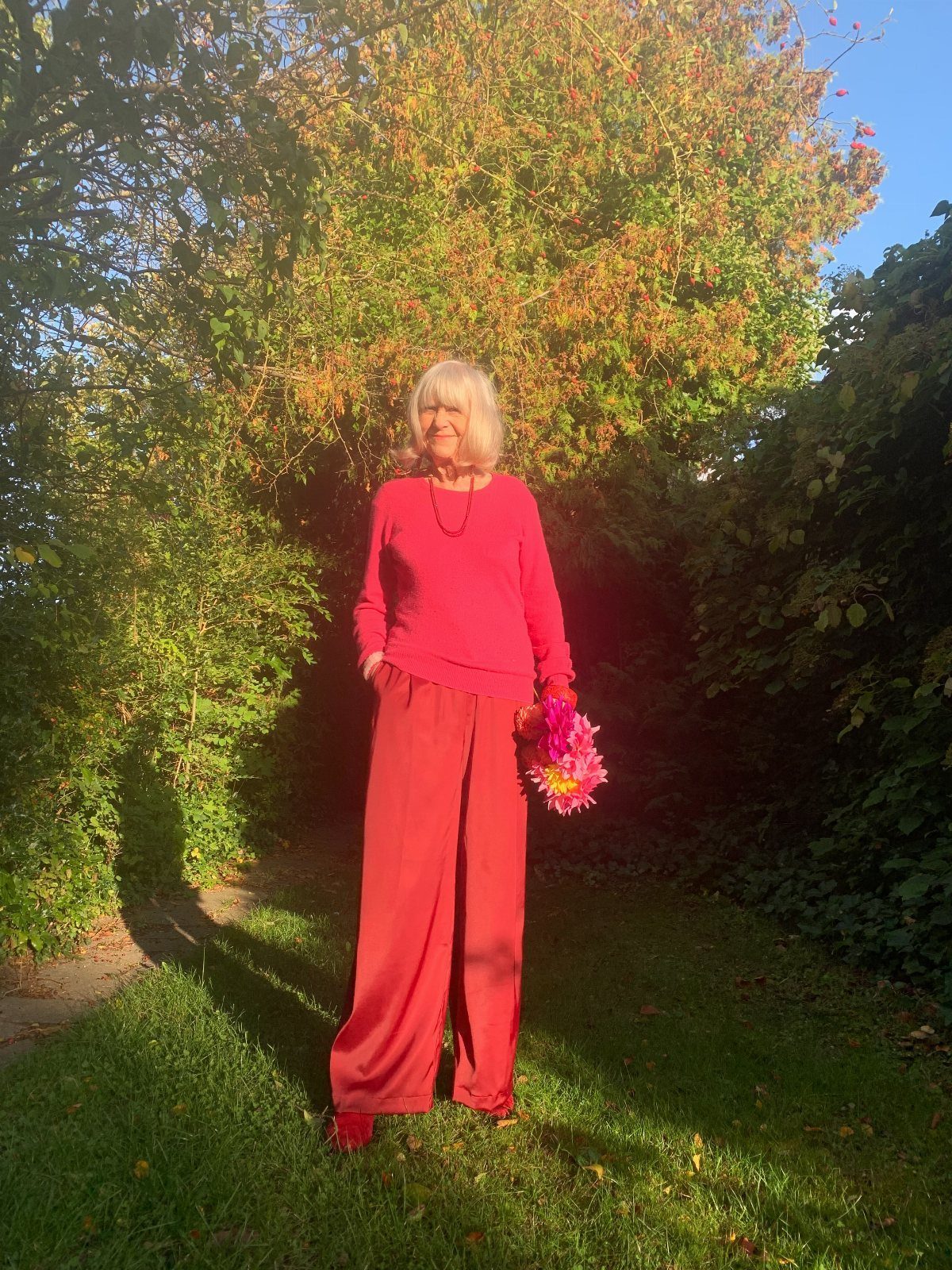 Swedish Women's Clothing Ideas: 8 Outfits to Wear Now 6 Woman in pink top and red wide-leg trousers holding pink flowers outdoors.