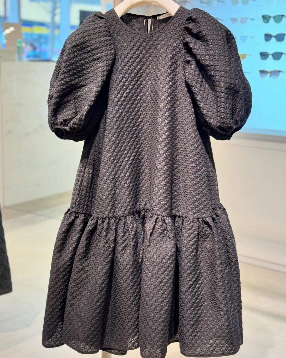 Swedish Women's Clothing Ideas: 8 Outfits to Wear Now 4 Black textured mini dress with puffed sleeves hanging in a bright clothing store.
