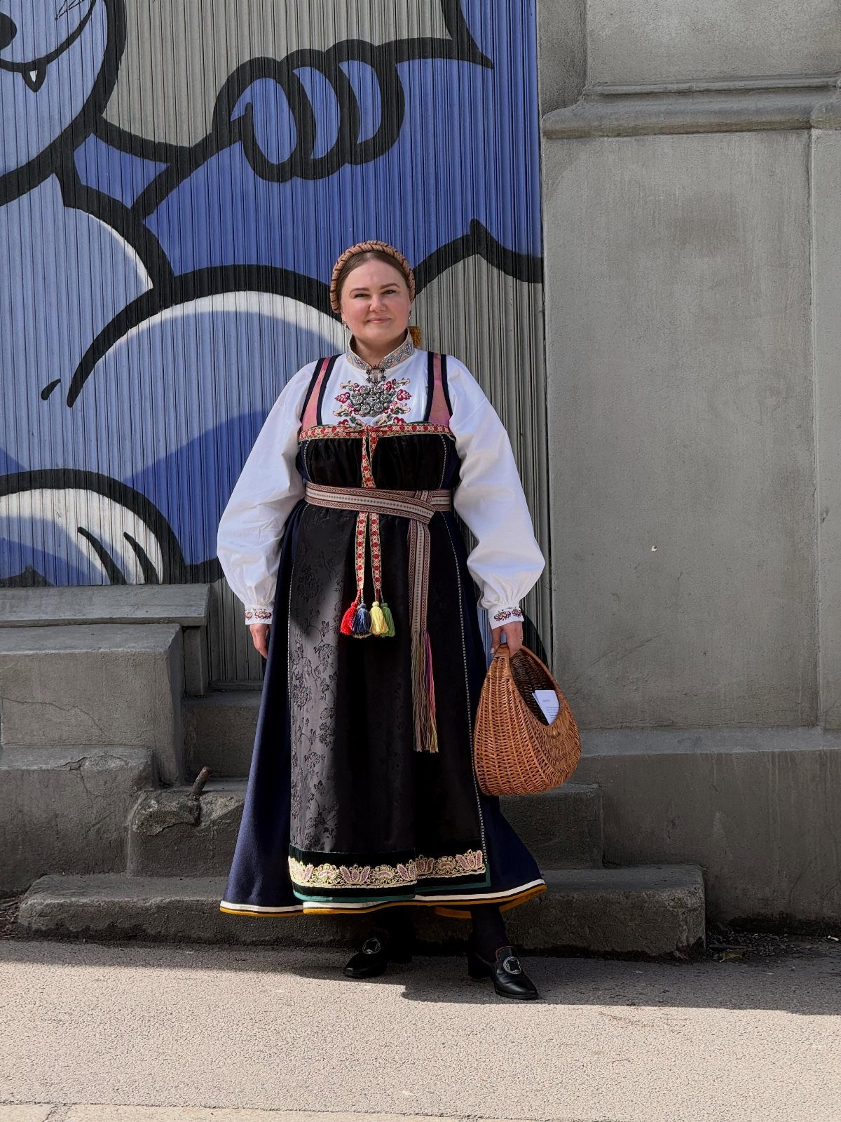 Woman in traditional Danish folk costume with black apron and gold embroidery holding basket