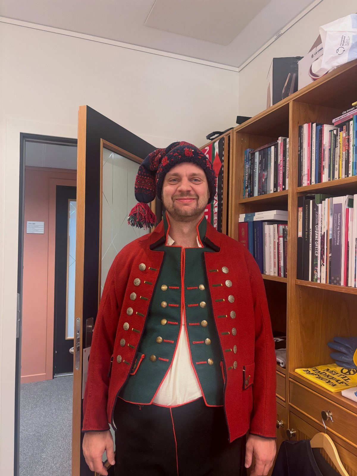 Man in traditional red and green Danish clothing wearing a knitted tassel hat.