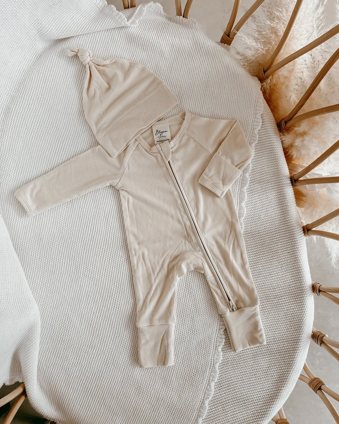 Cream ribbed baby zip footie and matching knotted beanie on a white blanket.