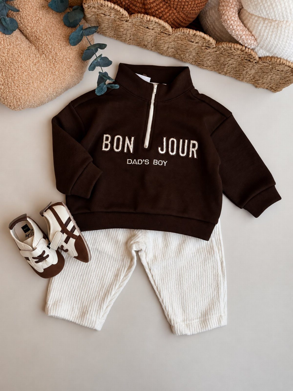 Brown baby sweatshirt and white ribbed pants with matching sneakers laid flat.