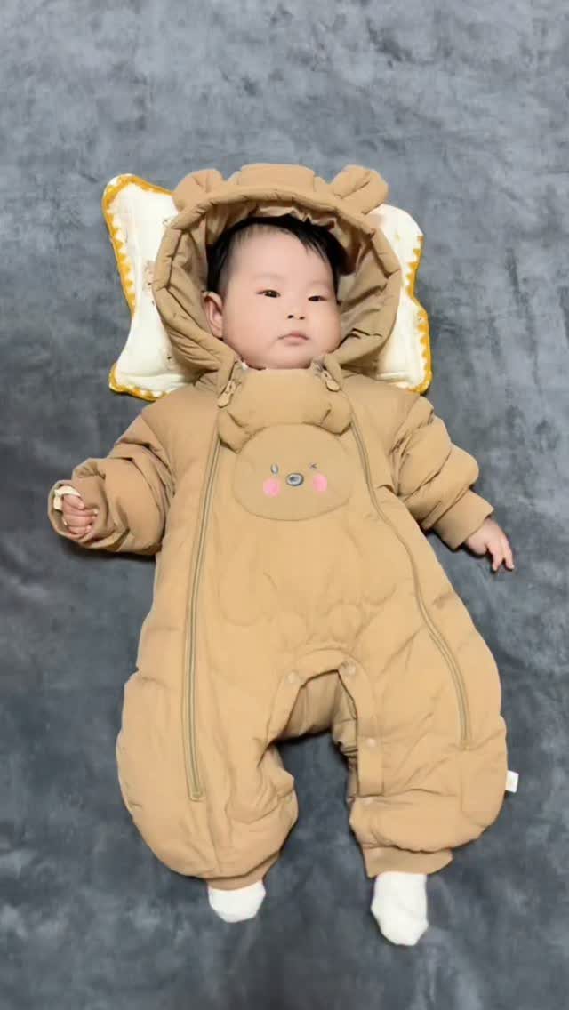 Newborn baby wearing a tan padded bear snowsuit lying on a grey blanket.