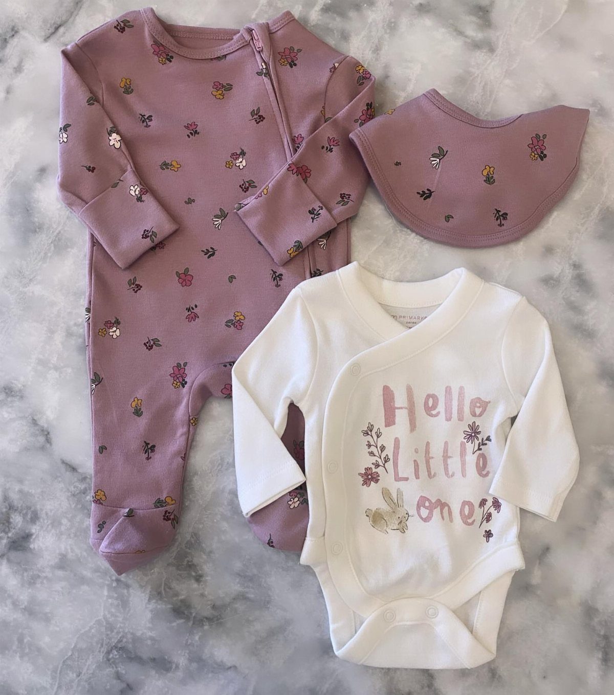 Baby clothing set including a mauve floral footie, bib, and white bodysuit.