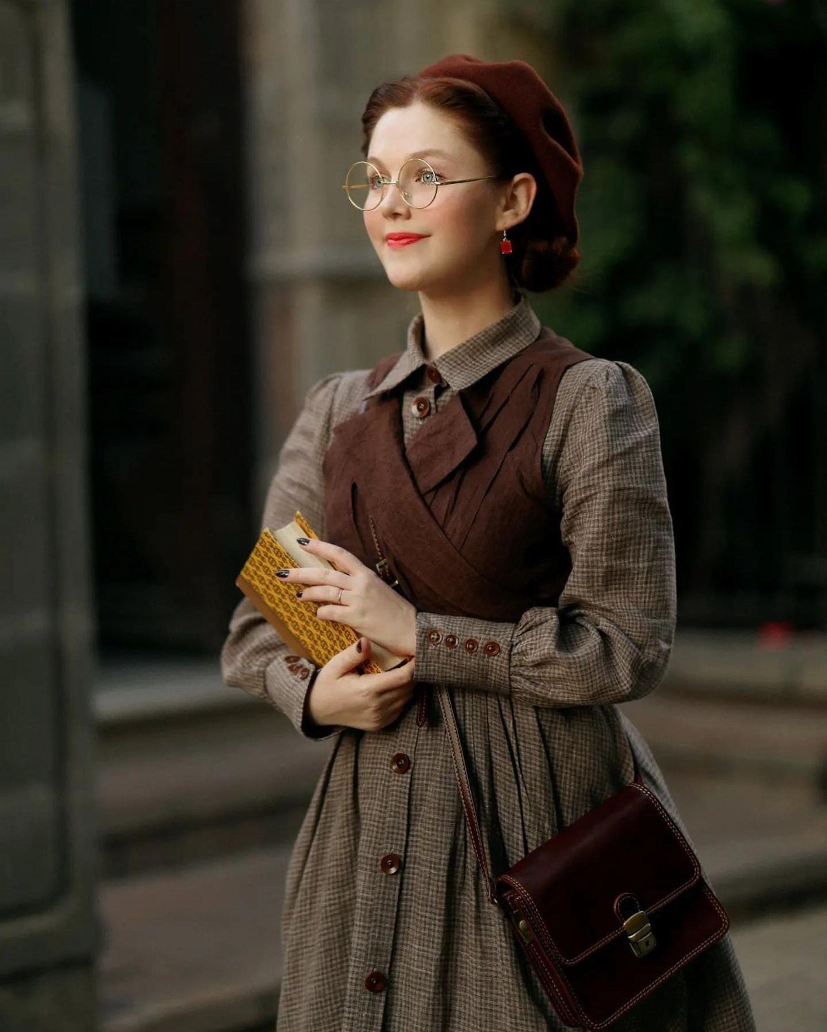 Woman in brown Victorian-style dress and red beret holding a yellow book.