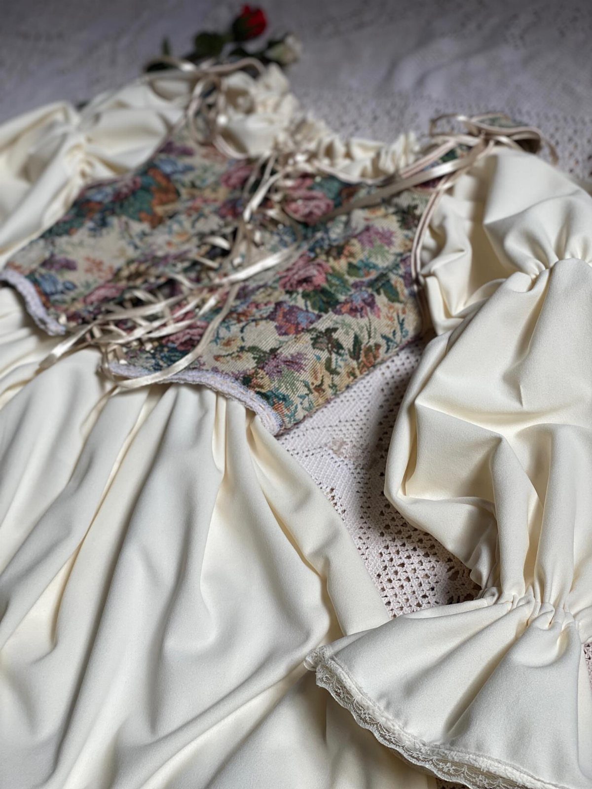 Victorian-style cream dress with floral laced bodice laid on white lace fabric