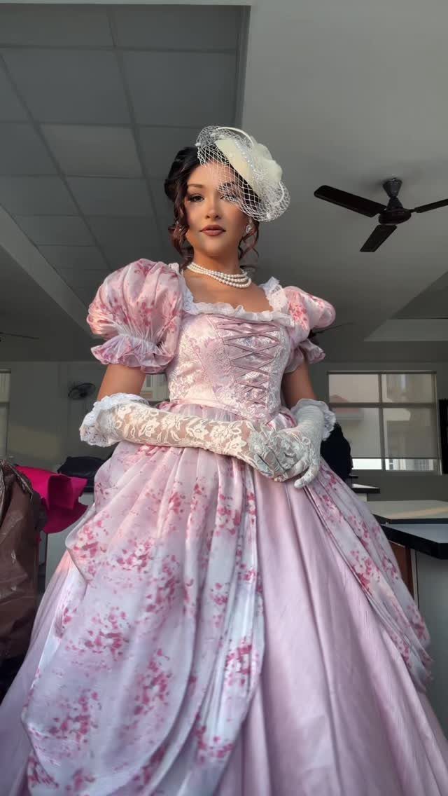 Woman in a pink floral Victorian gown with lace gloves and a fascinator.