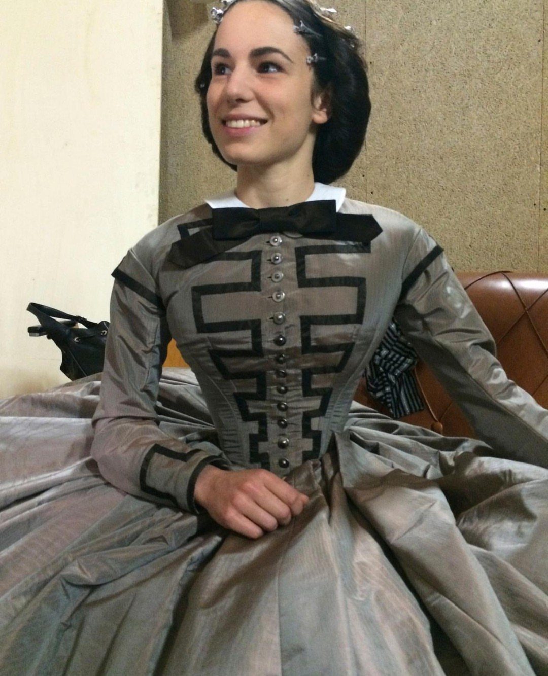 Woman in a grey Victorian dress with a structured bodice and full skirt.